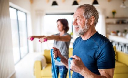 Older man and woman exercising at home with elastics and weights.